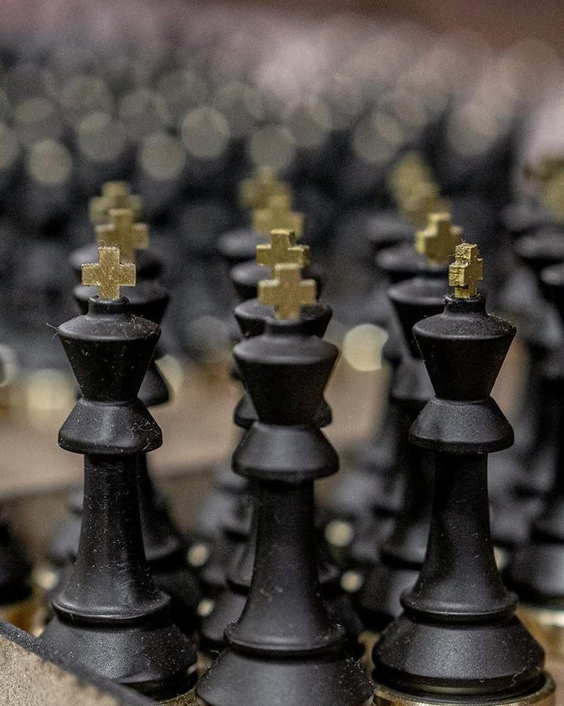 May include: Close-up of black chess pieces with gold-colored crosses on top. The pieces are arranged in rows, with a shallow depth of field. The focus is on the king pieces, which are in the foreground.