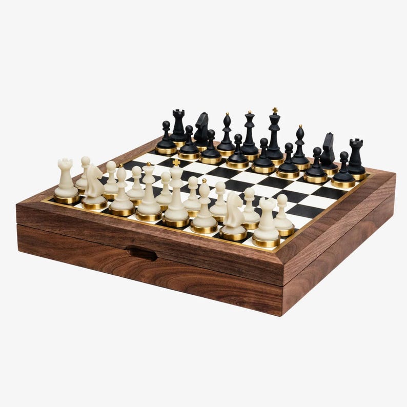 May include: A wooden chess set with black and white pieces arranged on a checkered board. The chess pieces are black and off-white, with gold-colored accents. The board is set inside a wooden box.