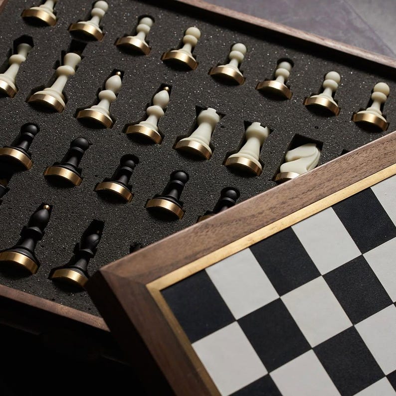 May include: A wooden chess set with a black and white checkered board. The chess pieces are stored in a foam-lined compartment. The pieces are black and white with gold-colored accents.