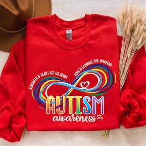 Peut inclure: Sweat-shirt rouge avec un symbole d'infini arc-en-ciel et le texte "Strength & heart set us apart. Love & embrace the amazing. Autism awareness."