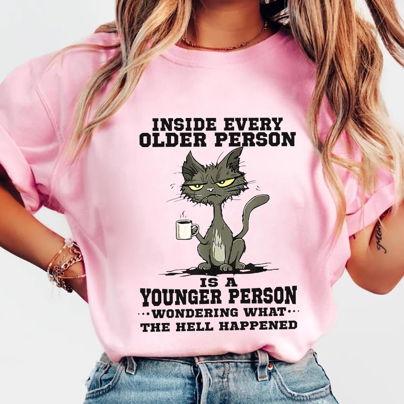 A woman wearing a pink t-shirt with a cartoon cat and text that reads "Inside every older person is a younger person... wonder what happened".