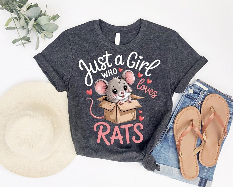 a gray t-shirt with a cartoon mouse inside a cardboard box, accompanied by the text "Just a Girl who loves Rats". The t-shirt is laid out on a white background, along with a hat, a pair of jeans, and a pair of sandals.