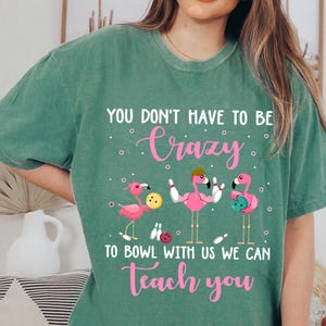 May include: Green t-shirt with a pink flamingo bowling graphic and the text "You don't have to be crazy to bowl with us we can teach you."