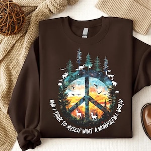 May include: Brown sweatshirt with a peace sign graphic surrounded by trees, animals, and a sunset. The text "And I think to myself what a wonderful world" is printed around the peace sign.