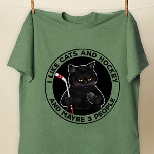 a green t - shirt with a black cat holding a toothbrush