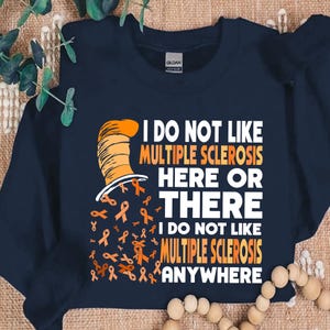 May include: A navy blue sweatshirt with a white graphic of a cat wearing a hat. The graphic says "I do not like multiple sclerosis here or there. I do not like multiple sclerosis anywhere." Orange ribbons are scattered around the graphic.