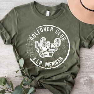 May include: A green t-shirt with a white graphic of a rollover club logo. The logo features a white silhouette of a vehicle on its side with the text "Rollover Club VIP Member".