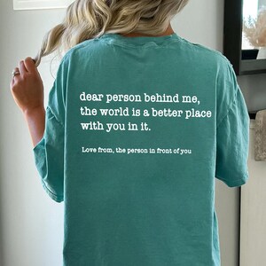 a woman wearing a t - shirt that says dear person behind me, the world