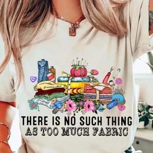 May include: White t-shirt with a colorful illustration of fabric, thread, needles, and other sewing supplies. The text "There is no such thing as too much fabric" is printed below the illustration.