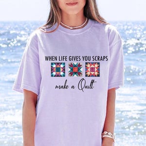 May include: A lavender t-shirt with the text "When life gives you scraps make a quilt" and three colorful quilt block designs.