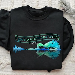 May include: Black sweatshirt with a blue and green watercolor design of a guitar and trees with the text "I got a peaceful easy feeling" on the front.