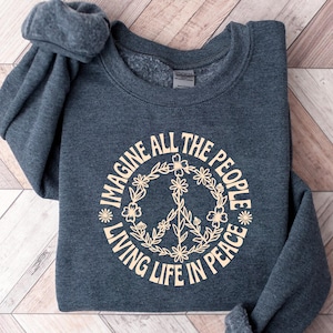 May include: A dark teal sweatshirt with the text "IMAGINE ALL THE PEOPLE LIVING LIFE IN PEACE" in a cream-colored floral design. The peace sign is in the center of the floral wreath.