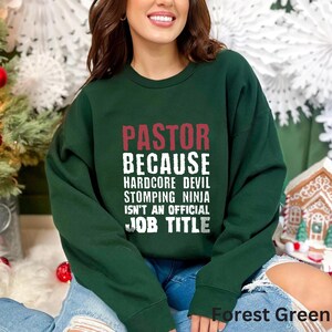 May include: Forest green sweatshirt with the text "PASTOR BECAUSE HARDCORE DEVIL STOMPING NINJA ISN'T AN OFFICIAL JOB TITLE" in white.