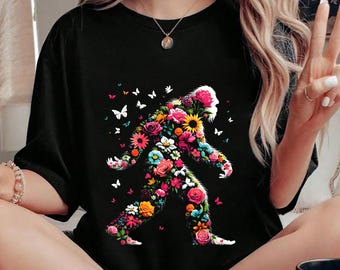 May include: Black t-shirt with a graphic of a Bigfoot silhouette made of colorful flowers and butterflies.