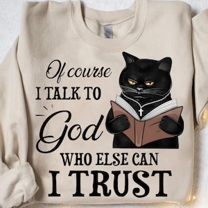 May include: A black cat wearing a beaded necklace and holding a book with a cross on the cover. The text on the image reads "Of course I talk to God who else can I trust".