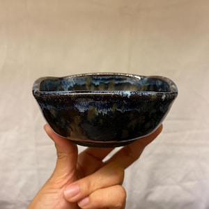 Peut inclure: Un petit bol en céramique de forme carrée avec un glaçage bleu foncé et brun. Le glaçage a un effet marbré, avec des stries blanches et dorées.