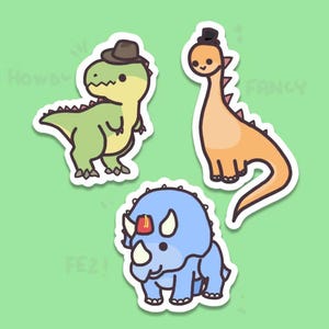 May include: Set of three dinosaur stickers. One green dinosaur wearing a brown hat, an orange dinosaur with a black top hat, and a blue triceratops. The stickers are on a green background.