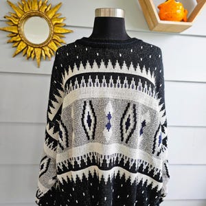 May include: A black, white, and gray patterned sweater displayed on a mannequin. The sweater features geometric designs, including zigzags and diamond shapes. The long-sleeved sweater has a crew neck and a relaxed fit, perfect for a cozy, vintage look.
