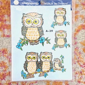 May include: A sheet of handpainted decals by Decorcal featuring five owls perched on branches with blue flowers. The owls have brown and tan feathers with large yellow eyes. The text HANDPAINTED DECALS by Decorcal and A-39 are printed on the top.