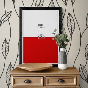 May include: A framed art print with the text "SHARE THE LOAD" above a graphic of two rings, set against a red and white background. The print is displayed on a wooden dresser with a decorative bowl and a vase with greenery.