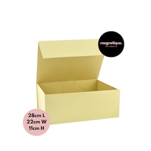 Peut inclure: Une boîte cadeau rectangulaire jaune pâle avec un couvercle ouvert. La boîte mesure 28 cm de long, 22 cm de large et 11 cm de haut. La marque "magnetique" est affichée sur un cercle noir.