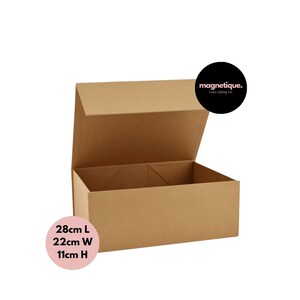Puede incluir: Una caja de cartón marrón con cierre magnético. La caja está abierta y la tapa está levantada. La caja mide 28 cm de largo, 22 cm de ancho y 11 cm de alto. El texto "magnetique. Ease Gifting Co." está impreso en una pegatina circular negra en la tapa.