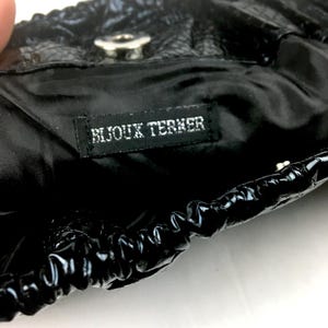 Puede incluir: Bolso negro con cierre de cord&oacute;n y un bot&oacute;n plateado. El bolso tiene una etiqueta negra que dice "Bijoux Terner".