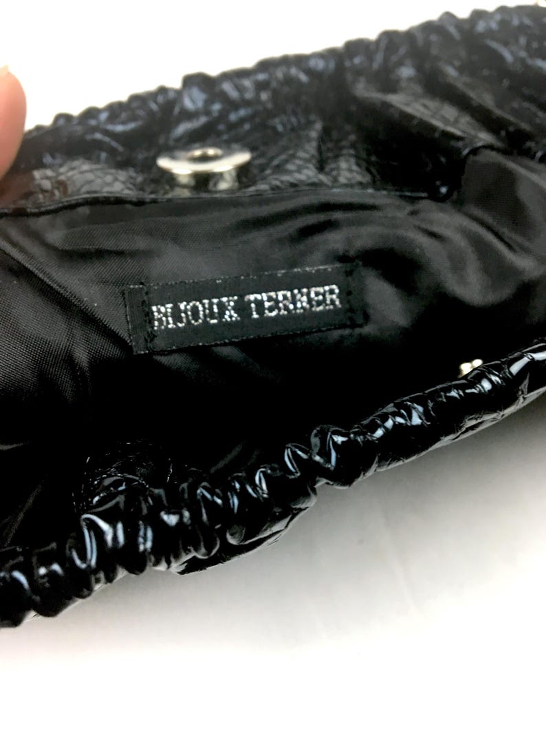 Puede incluir: Bolso negro con cierre de cord&oacute;n y un bot&oacute;n plateado. El bolso tiene una etiqueta negra que dice "Bijoux Terner".