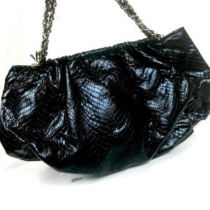 Puede incluir: Un bolso de mano negro con estampado de piel de serpiente y una correa de cadena plateada.
