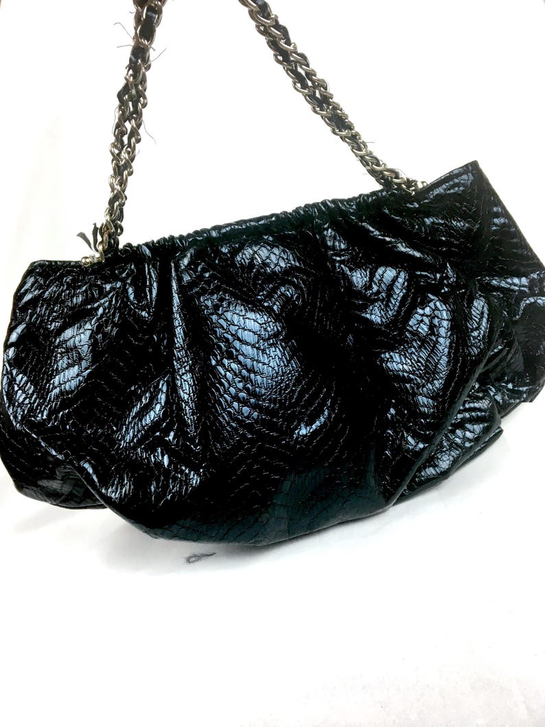 Puede incluir: Un bolso de mano negro con estampado de piel de serpiente y una correa de cadena plateada.