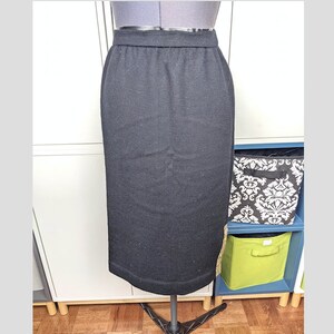 May include: A black pencil skirt made of a ribbed knit fabric. The skirt has an elastic waistband and a straight, knee-length hem. The skirt is displayed on a mannequin.