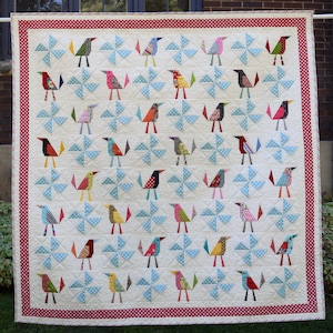 Peut inclure: Une courtepointe blanche avec une bordure à pois rouges et blancs. La courtepointe présente un motif répétitif de moulins à vent bleus et d'oiseaux stylisés colorés.