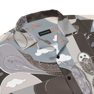 May include: A button-down shirt with a unique paisley and fish pattern in shades of gray, brown, and blue. The shirt features a collar and a label that reads "Fisherman Jac". The overall design is artistic and eye-catching.