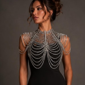 May include: A silver-toned rhinestone body chain necklace featuring multiple draped strands that extend from a high collar down across the chest and over the shoulders, creating a layered, cascading effect over a plain black sleeveless garment.