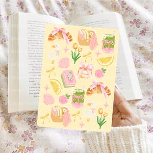 May include: A yellow sticker sheet featuring watercolor illustrations of croissants, books, ducks, flowers, and drinks. The sticker sheet has a light pink and green color scheme with bows and lemon slices.