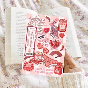 May include: A pink and white striped card with various illustrations and text, including a ticket that says "Spicy Romance Book Club" and the phrase "Call Me A Good Girl." Other images include a candle, a glass of wine, and a cake.