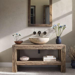 May include: A bathroom scene featuring a wooden vanity unit with a stone basin and a wooden-framed mirror. The vanity has a lower shelf with decorative items. A vase of flowers and a towel rail are also visible.