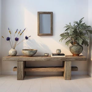 May include: A rustic wooden console table with a variety of decorative items. It features a large vase with leafy plants, a smaller vase with purple flowers, a wooden bowl, and a small mirror. The room has white walls and a light wood floor.
