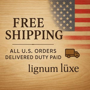 May include: A wooden background with the text "FREE SHIPPING" in a bold, dark brown font. The American flag is in the upper right corner. Below the text is "ALL U.S. ORDERS DELIVERED DUTY PAID" and the brand name "lignum l&uuml;xe".