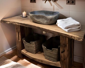 May include: A bathroom vanity featuring a live-edge wooden countertop and a natural stone vessel sink. Below the counter, two woven baskets sit on a lower shelf. A white folded towel rests on the counter next to a lit candle in a glass holder.