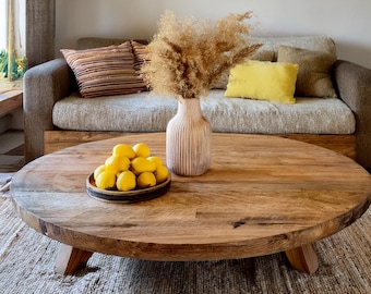 May include: A round wooden coffee table with short legs, featuring a ribbed ceramic vase filled with dried pampas grass and a small dark bowl containing a cluster of bright yellow lemons, positioned in a living space.