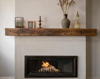 May include: A rustic fireplace with a wooden mantel holding decorative items. A terrarium, framed art, a candlestick, a vase with dried plants, and a birdcage are displayed. The fireplace has a black frame and a fire burning inside.