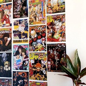 May include: A white wall with a collection of colorful anime magazine covers featuring characters from popular series like "Attack on Titan", "Hunter x Hunter", "Banana Fish", and "My Hero Academia".