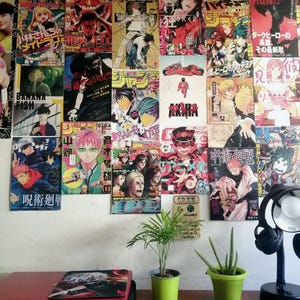 May include: A wall covered in colorful anime posters, with a laptop, two potted plants, and a desk lamp on a wooden table in the foreground.