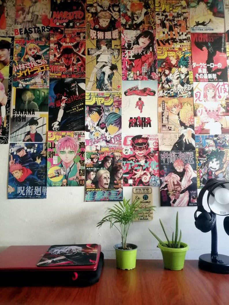 May include: A wall covered in colorful anime posters, with a laptop, two potted plants, and a desk lamp on a wooden table in the foreground.