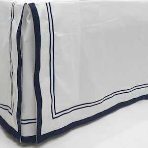 Może przedstawiać: Biała spódnica do łóżka z granatową lamówką. Lamówka ma dwie granatowe linie wokół krawędzi spódnicy.