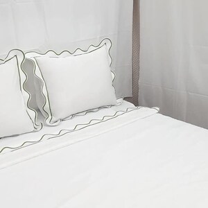 May include: White bedding set with green scalloped trim. The set includes two pillows and a fitted sheet. The pillows and sheet have a decorative green trim. The bed is made and ready for use.