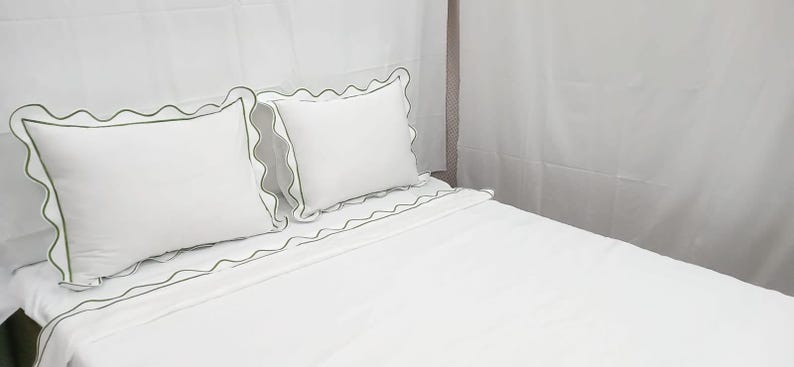 May include: White bedding set with green scalloped trim. The set includes two pillows and a fitted sheet. The pillows and sheet have a decorative green trim. The bed is made and ready for use.