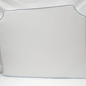 May include: A white rectangular headboard with a light blue trim. The headboard has a curved top edge and is made of a soft, padded material. The headboard is designed for a bed.