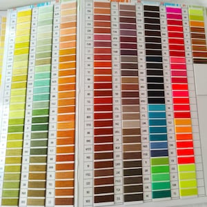 May include: A color chart for embroidery floss, featuring a wide array of hues. The chart displays organized rows of thread samples, ranging from vibrant yellows and greens to deep reds and blues. Each color is labeled with a number.